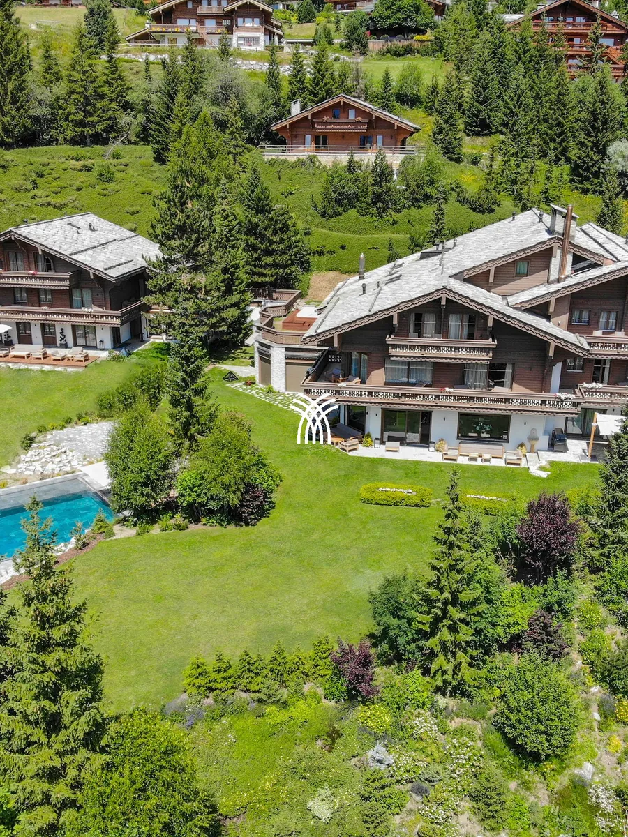 Aerial view of Chalet Christiana on green lawns in the pine forest of Crans-Montana, in summer.