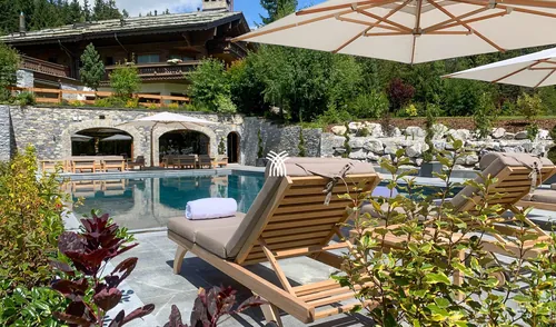 The summer pool terrace of Chalet Christiana, with sunloungers and a parasol.