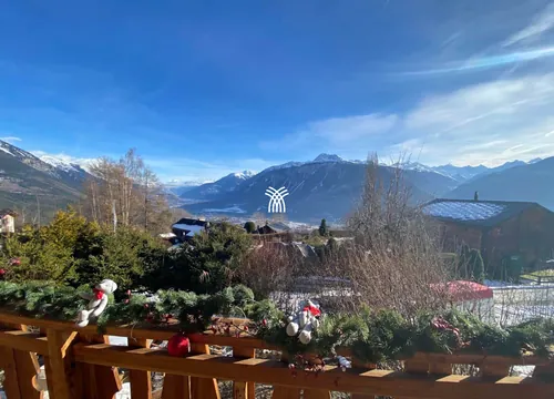 The terrace of Chalet Cervo with red flowers, overlooking the valley in summer.