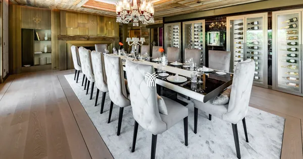 The dining room of Chalet Christiana in Crans-Montana, with a long white table, crystal chandelier and a wine wall.